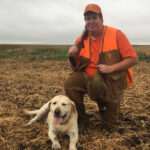 Jimmy Argent, originally of Steele, N.D. pauses with the author’s lab Ole and a mature rooster, following a hunt down the small drain pictured in the back. Reserving marginal acres amidst cropland provides valuable habitat for wildlife and hunting opportunities. Simonson Photo.